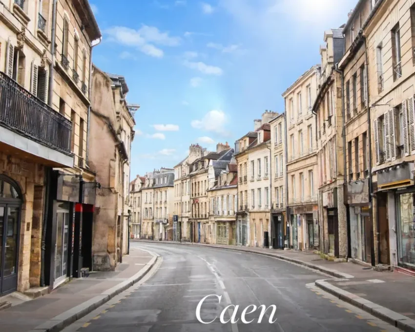 Vue d'une rue caennaise bordée de bâtiments en pierre, volets blancs et balcons en fer, boutiques au rez-de-chaussée, ciel bleu.