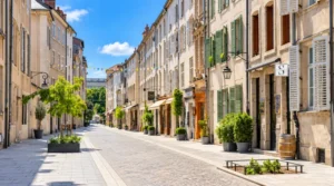 vue d une rue pietonne bordee d immeubles a facade beige, volets verts et plantes en pots, guirlandes a fanions