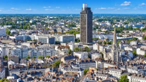 Plan aerien sur une ville dense avec une tour sombre au centre et une eglise gothique a droite, toits rouges et arbres.